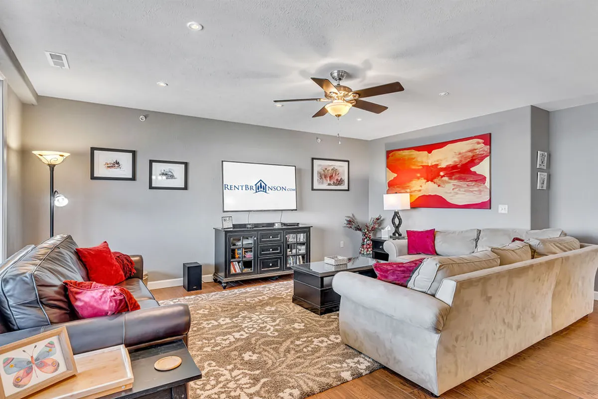 The hero image showcases a warm, inviting living room with plush sofas arranged for conversation, a large television, tasteful artwork, and a softly glowing lamp. The space is spacious and cozy, perfect for relaxing after a day on Table Rock Lake or gathering with family and friends.