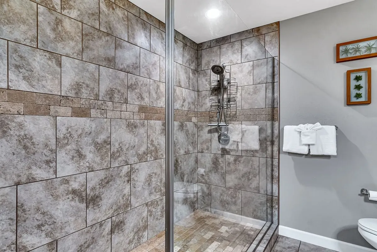A luxurious bathroom with a glass shower enclosure, textured tile walls, modern shower fixtures, and plush white towels. The spa-inspired design invites relaxation and self-care after a busy day.