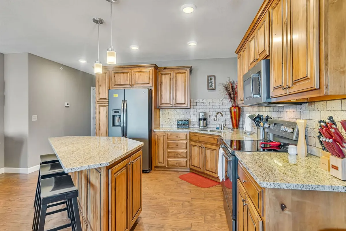 A sunlit kitchen with gleaming granite countertops, rich wooden cabinetry, a spacious kitchen island, and modern stainless steel appliances. The layout is open and inviting, offering plenty of space for meal preparation and group gatherings.