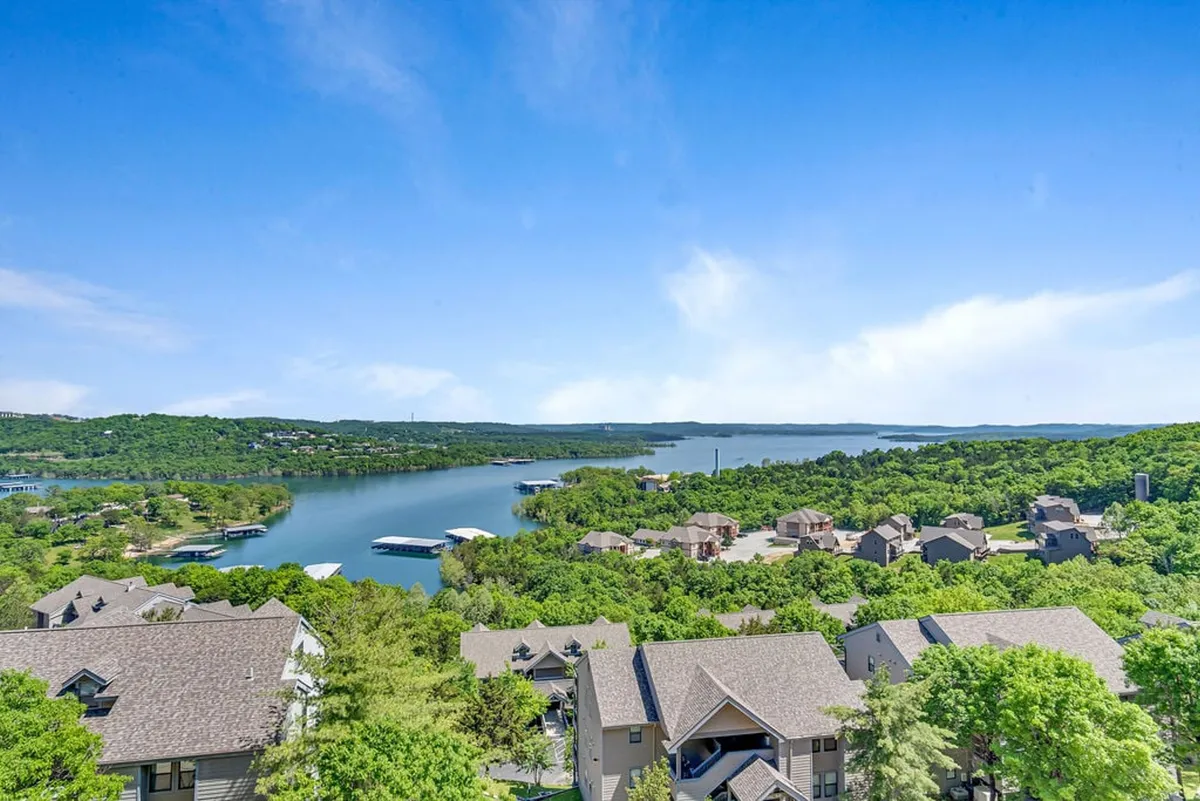 A picturesque view of sparkling lake waters framed by lush green trees and distant hills. Homes dot the shoreline, and the tranquil atmosphere invites boating, fishing, and lakeside relaxation. The image speaks to outdoor activities and panoramic lake vistas.