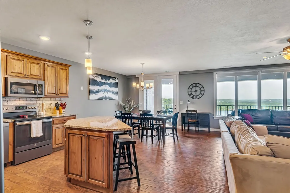 An open-concept interior with a kitchen island, adjacent dining table, and comfortable living room seating. Large windows flood the space with natural light, and the seamless flow between spaces embodies the open layout described in the section.