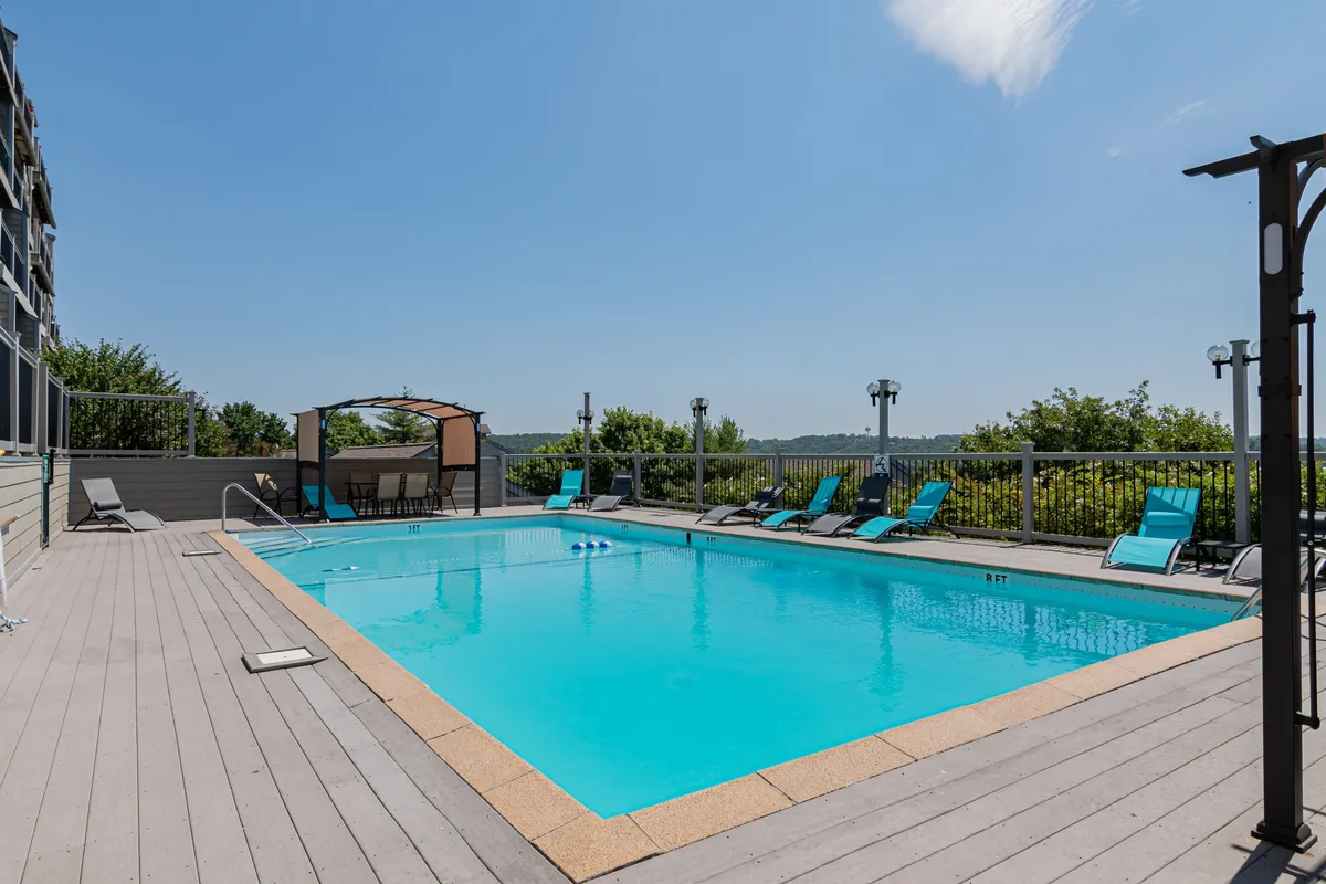 A vibrant exterior view of the resort's swimming pool area, complete with lounge chairs, a shaded canopy section, and clear blue water. The surroundings are designed for both relaxation and socializing, embodying the resort’s leisurely, vacation-ready feel.