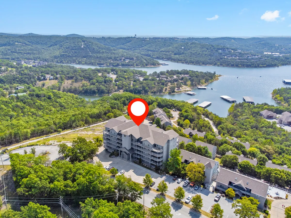 This exterior image features the apartment building set against lush greenery with a clear view of the lake in the background. The scene evokes a sense of serenity and direct access to Table Rock Lake, highlighting the proximity of the property to lakeside adventures, water activities, and scenic trails.