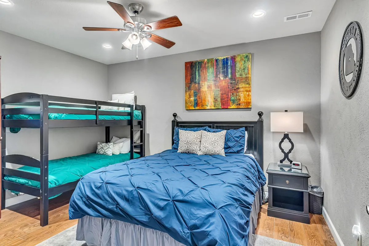 A cozy, family-friendly bedroom with a queen bed adorned with decorative pillows, a bunk bed perfect for kids, colorful wall art, and a nightstand with a lamp. The setup is both inviting and practical for families traveling with children.