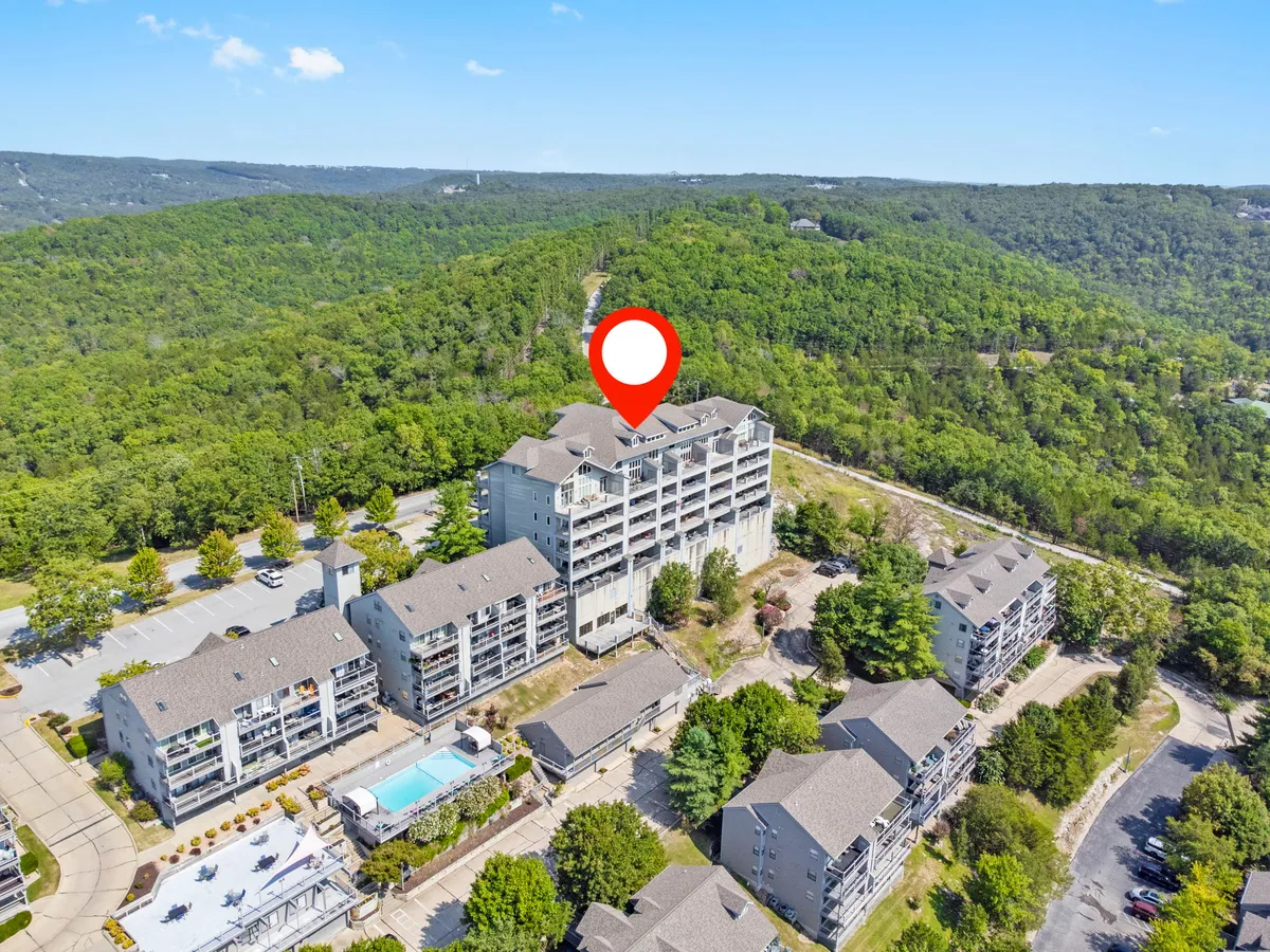 This exterior image highlights a tranquil swimming pool surrounded by green hills and residential buildings. The peaceful resort grounds, visible pool, and nearby nature trails suggest easy, step-free access to outdoor amenities and communal spaces.