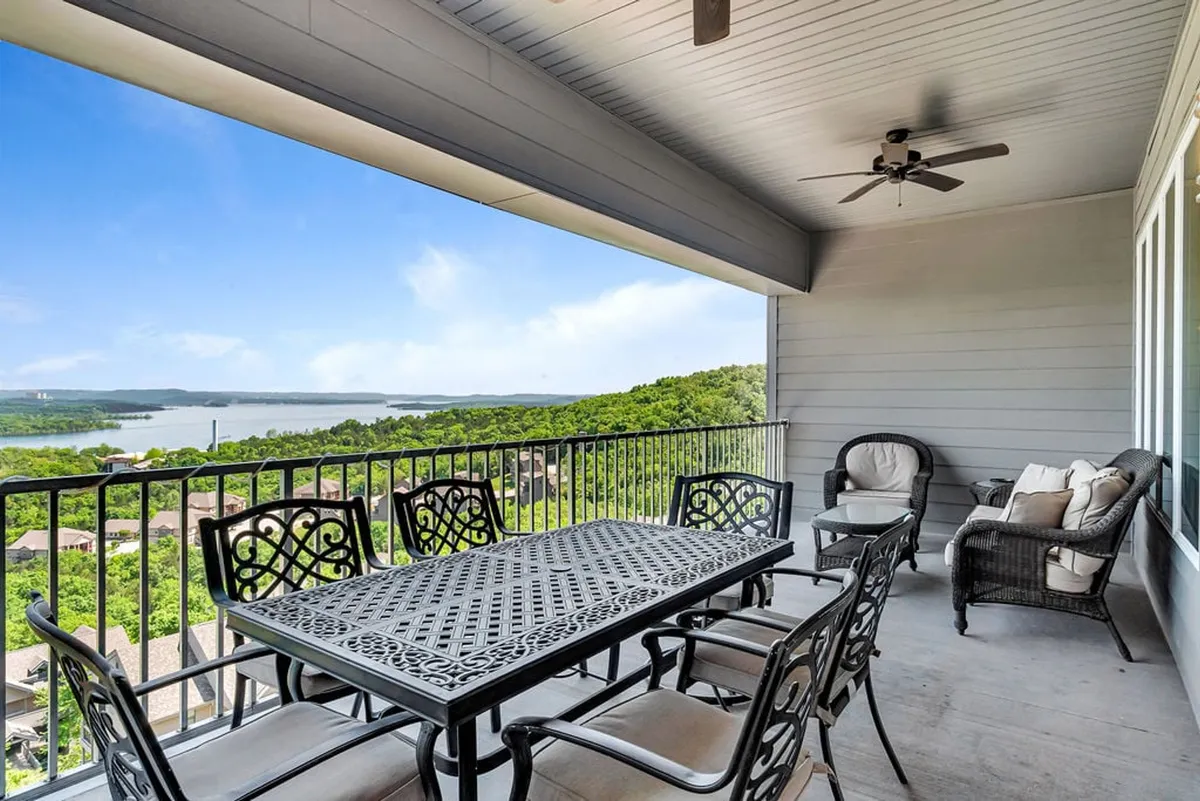 An exterior deck scene with a dining table, balcony railing, and comfortable outdoor seating. The view extends over the surrounding landscape, inviting guests to enjoy morning coffee, evening drinks, or lively conversations while overlooking Table Rock Lake.